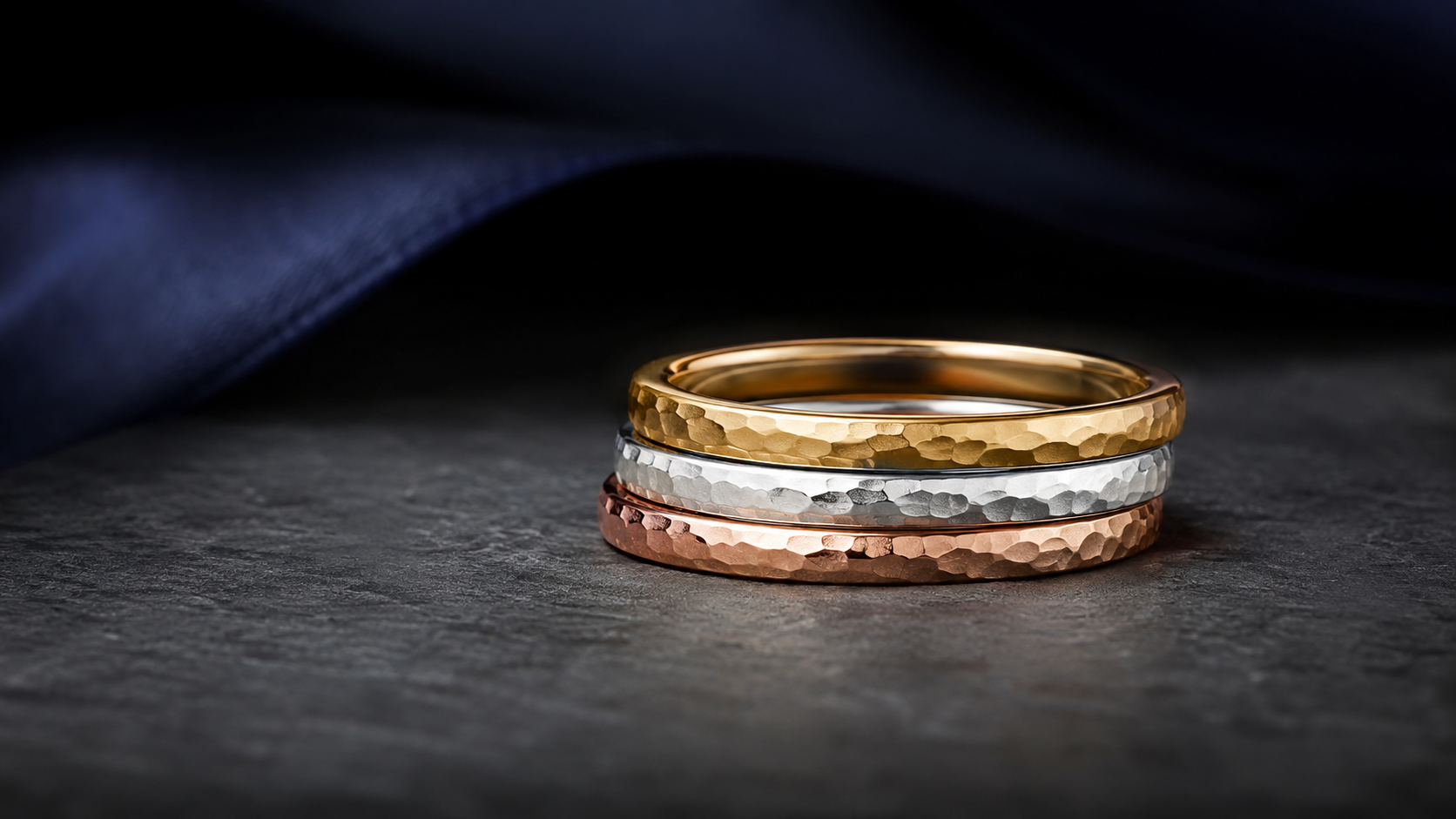 A stack of three thin rings in yellow, white and rose gold on a grey stone surface