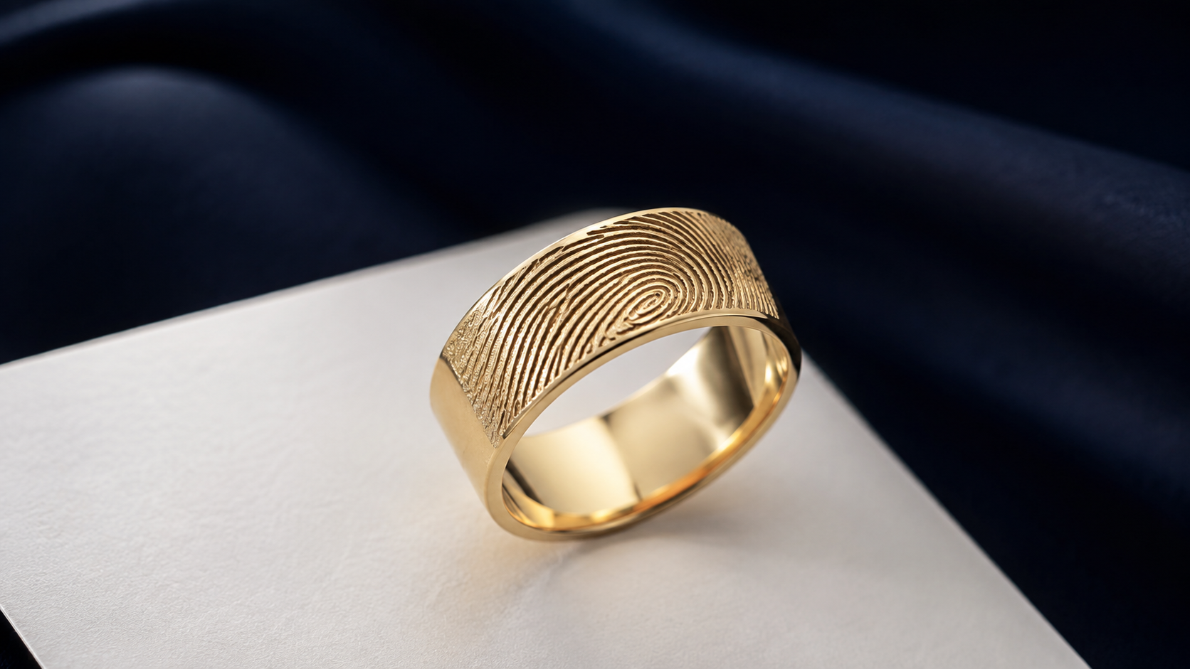 A wide gold band showing a fingerprint pattern laser-engraved on its outer surface, resting on white card